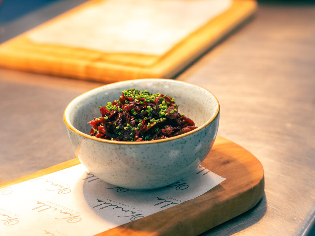 Fresh beetroot salad topped with chopped chives served in a ceramic bowl on a wooden board.