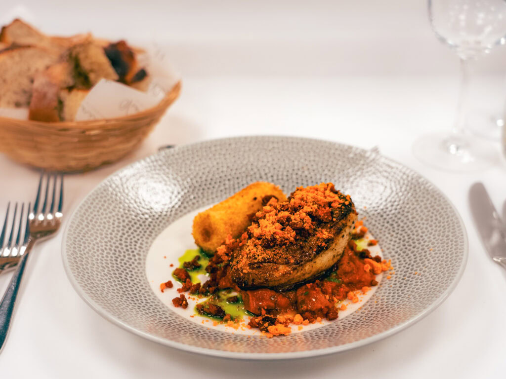 Delicious gourmet dish featuring crispy-crusted meat with vegetable sauce and side, served on elegant dinnerware.