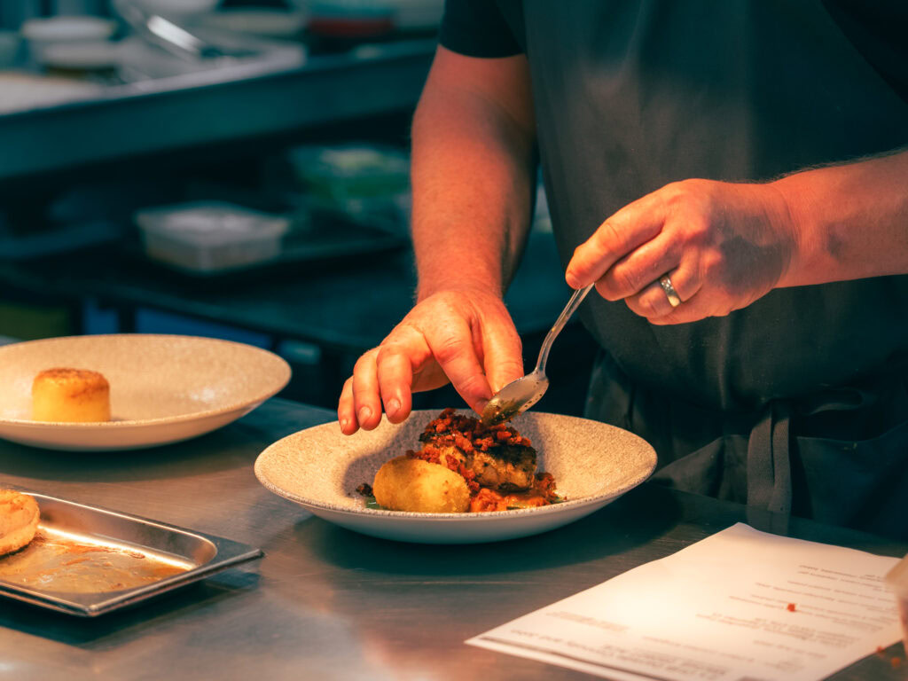 Delicious plated gourmet dish being carefully garnished in a professional kitchen setting.