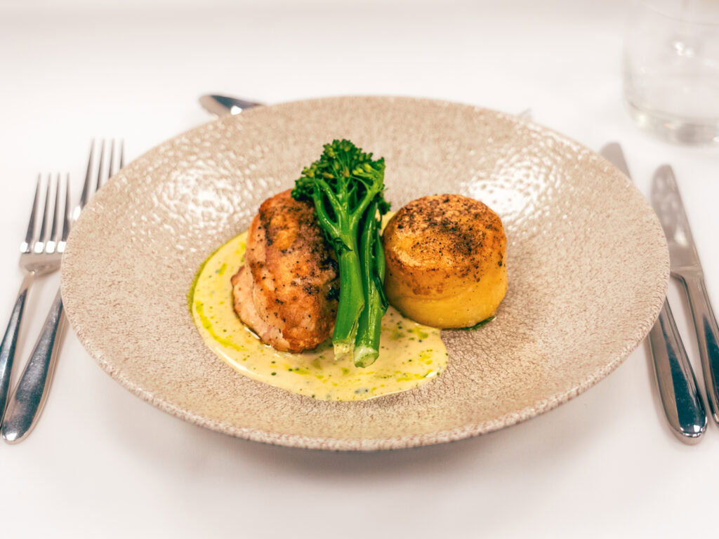 Succulent chicken roulade with greens, served with yellow potato and creamy sauce on textured beige plate.