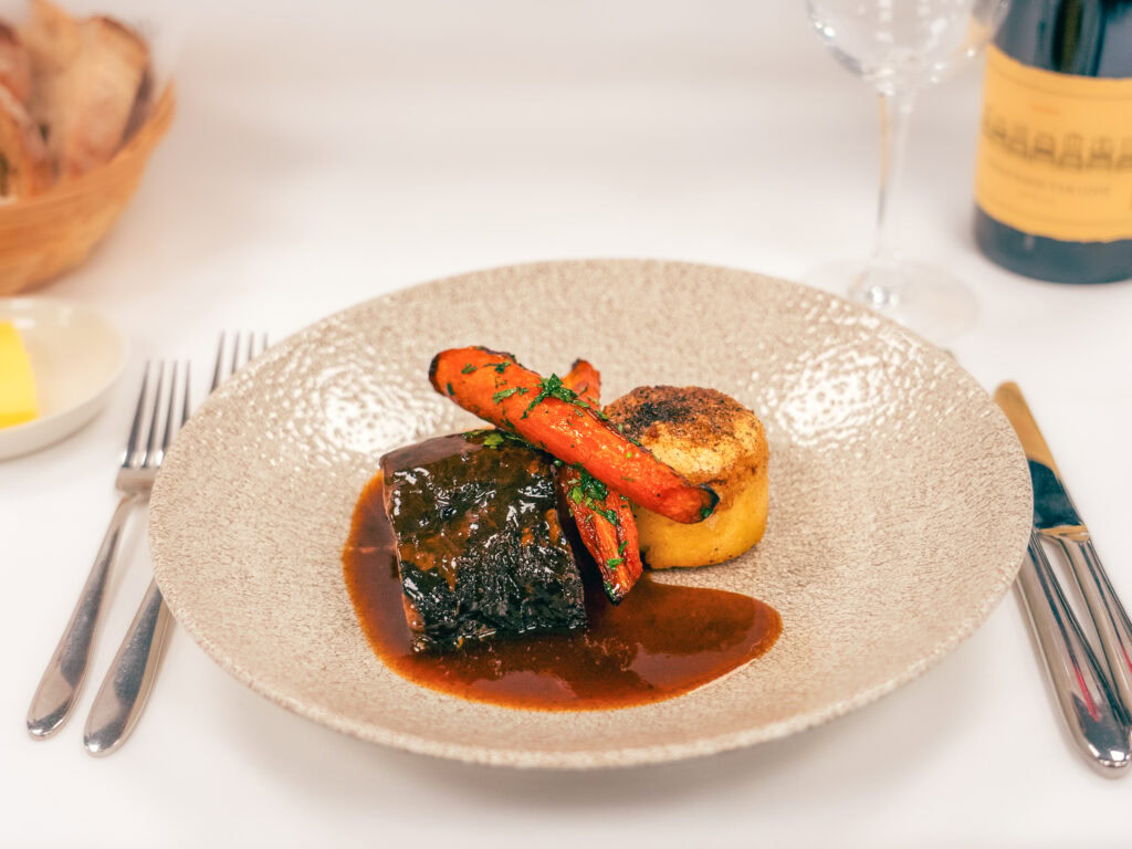 Succulent beef with roasted vegetables and rich gravy on an elegant beige plate in a fine dining setting.