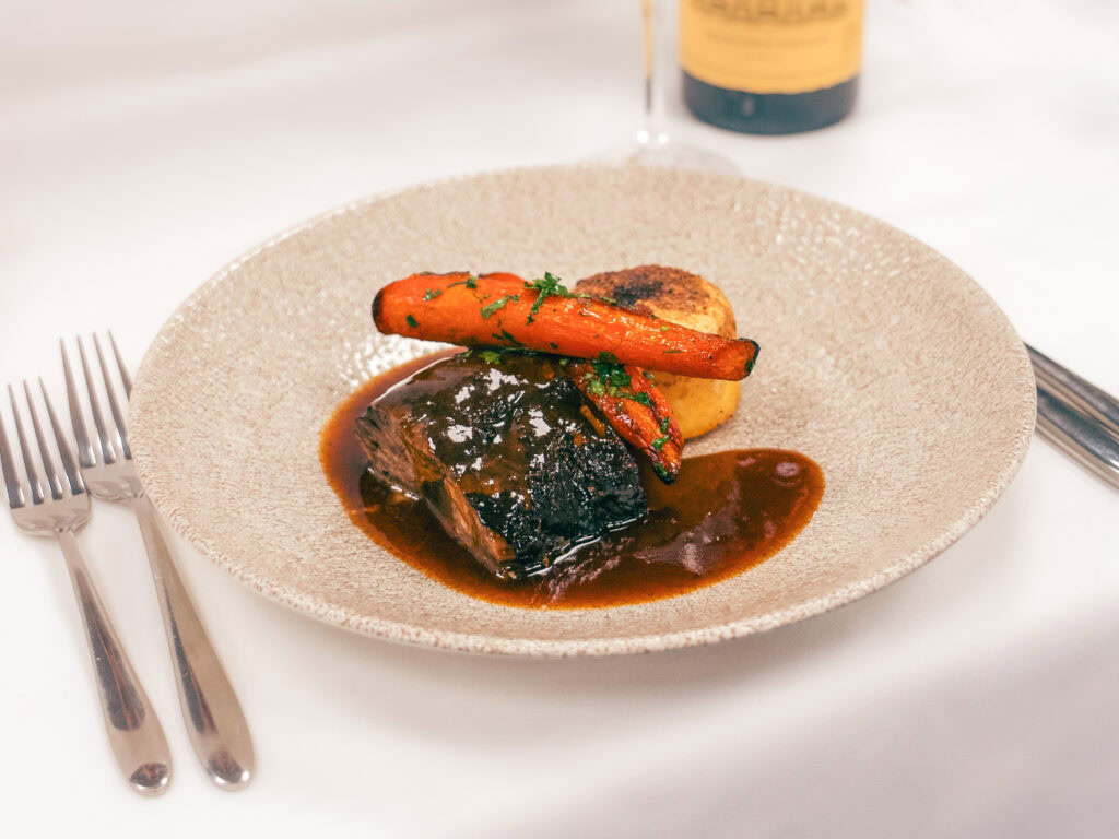 Slow-cooked beef with roasted carrots, potatoes, and rich gravy on elegant table setting.