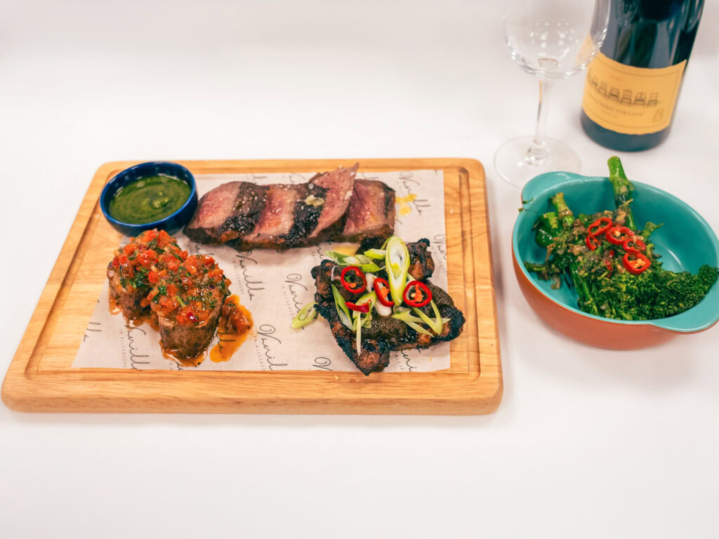 Succulent grilled steak with sauces, garnished vegetables, and fresh greens, served on a wooden platter.
