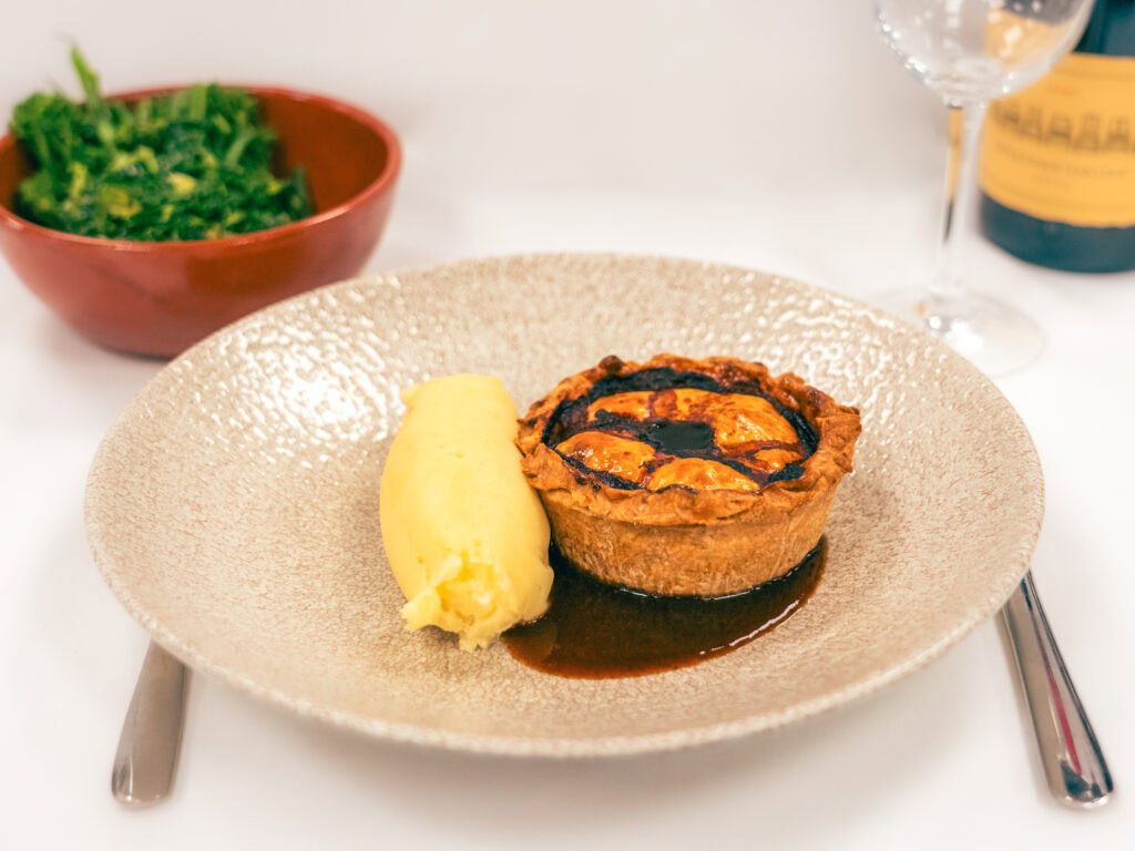 Creamy mashed potato with sticky toffee pudding and caramel sauce on a textured beige plate.