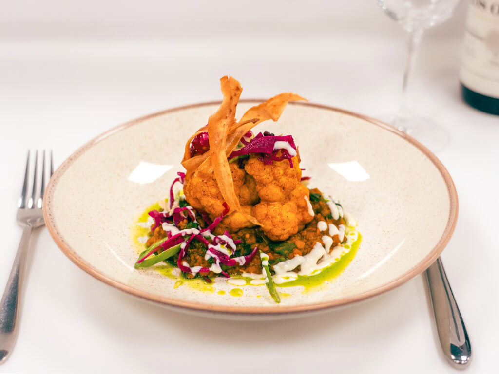 Delicious fried cauliflower with vibrant salads and curry sauce on a white dinner plate.
